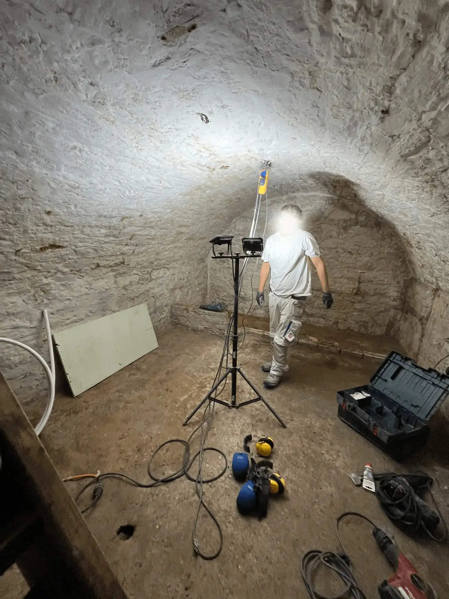 ein bauarbeiter im kellergewölbe mit werkzeug helm und einer kopflampe
